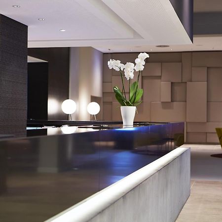 Steigenberger Hotel Am Kanzleramt Берлін Екстер'єр фото The photo shows a modern and stylish interior space, likely a hotel lobby or reception area. There is a sleek, dark countertop with a minimalist design, complemented by a decorative white vase containing white orchids. In the background, there are so