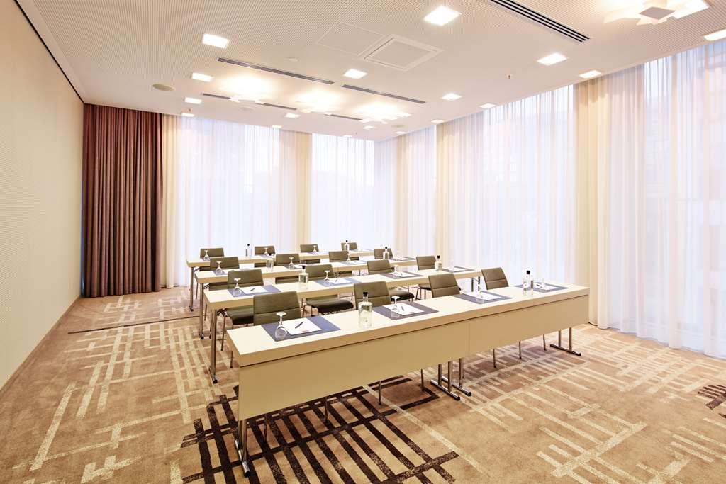 Steigenberger Hotel Am Kanzleramt Берлін Зручності фото The photo shows a modern conference room. It features several tables arranged in a U-shape, each equipped with notepads and pens. The room has large windows covered with sheer curtains, allowing natural light to fill the space. The walls are light-co