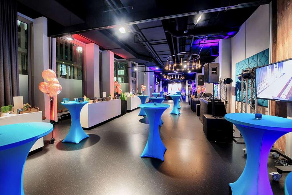 Steigenberger Hotel Am Kanzleramt Берлін Зручності фото The photo shows a spacious event venue with modern decor, featuring several tall, round tables covered in blue tablecloths. The area is well-lit with a combination of soft ambient lighting and colorful spotlights, creating a vibrant atmosphere. There
