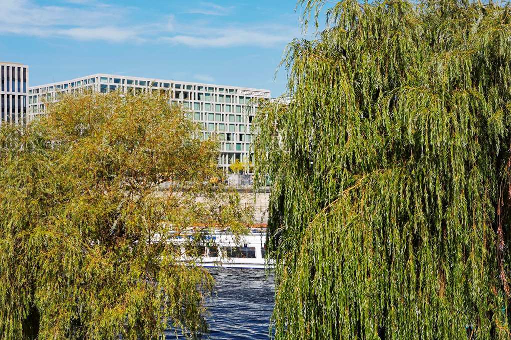 Steigenberger Hotel Am Kanzleramt Берлін Екстер'єр фото The photo shows a view with lush, green willows in the foreground, characterized by their long, drooping branches. In the background, there is a modern building with large windows, suggesting a contemporary architectural style. The scene also include