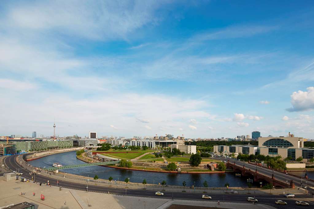 Steigenberger Hotel Am Kanzleramt Берлін Екстер'єр фото The photo depicts a panoramic view of a cityscape featuring a river that winds through the landscape. On one side of the river, there are green spaces with trees and grass, suggesting an area designed for leisure or parks. Along the riverbank, you ca