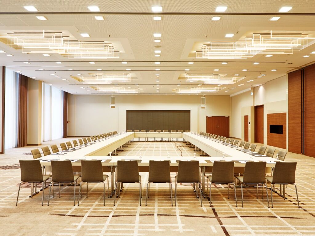 Steigenberger Hotel Am Kanzleramt Берлін Екстер'єр фото The photo shows a large, modern conference room designed for meetings or presentations. It features a long, rectangular table set up in the center, surrounded by multiple chairs. The room is well-lit with contemporary lighting fixtures on the ceiling